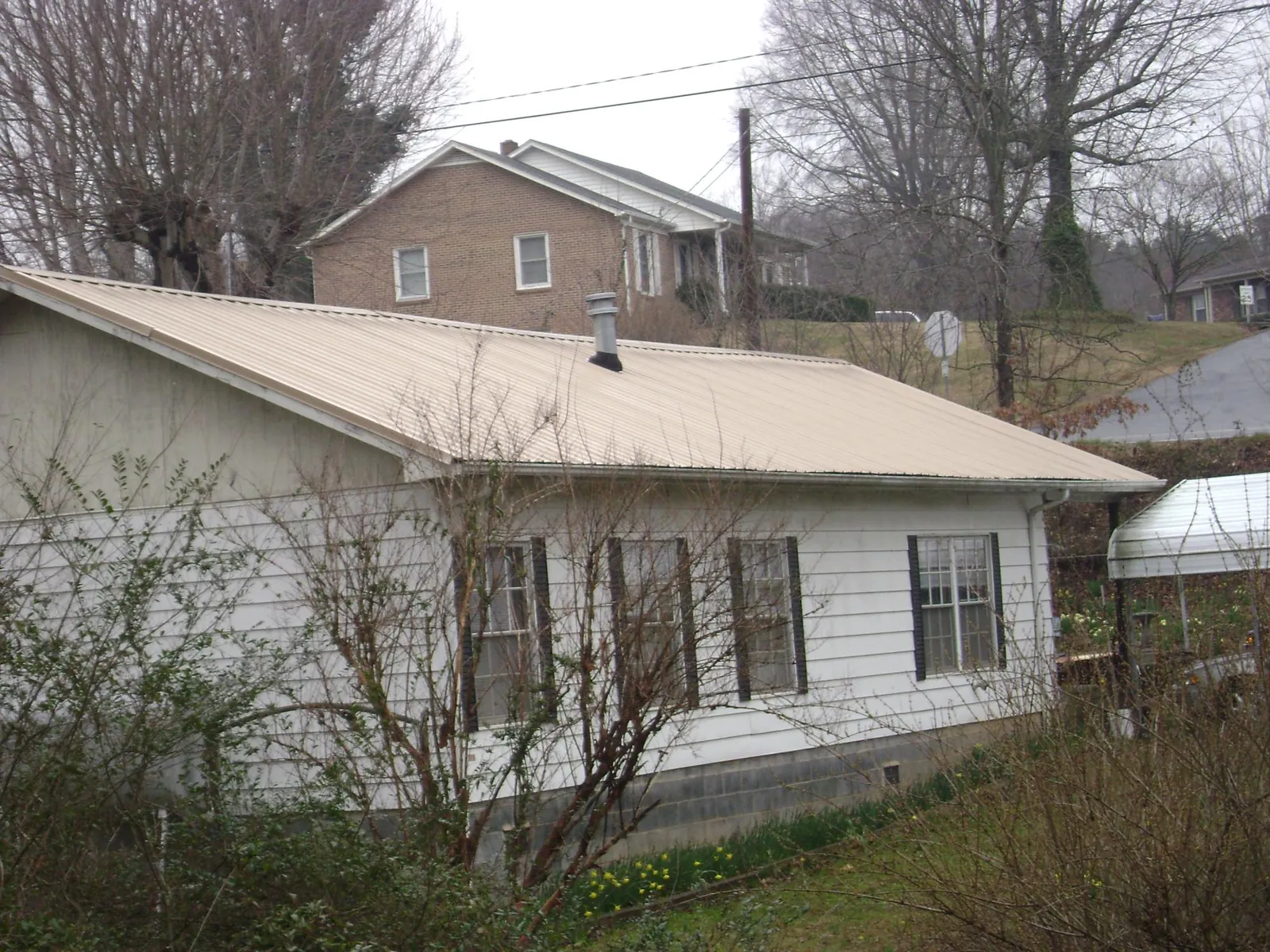 Tan metal roof on a white sided house set into a hillside in Fairfield